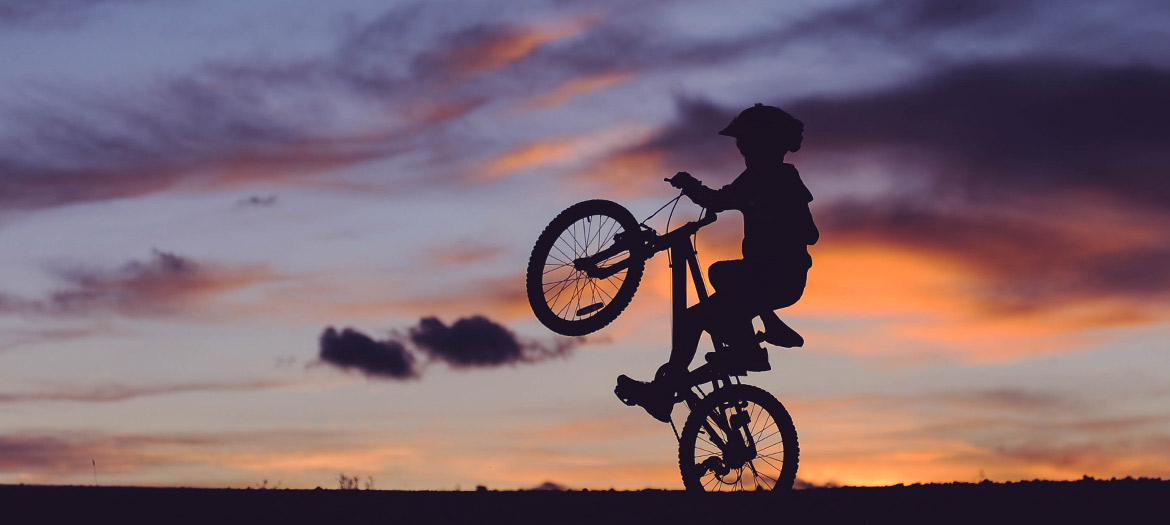 Silhouette of kid on mountain bike doing wheelie
